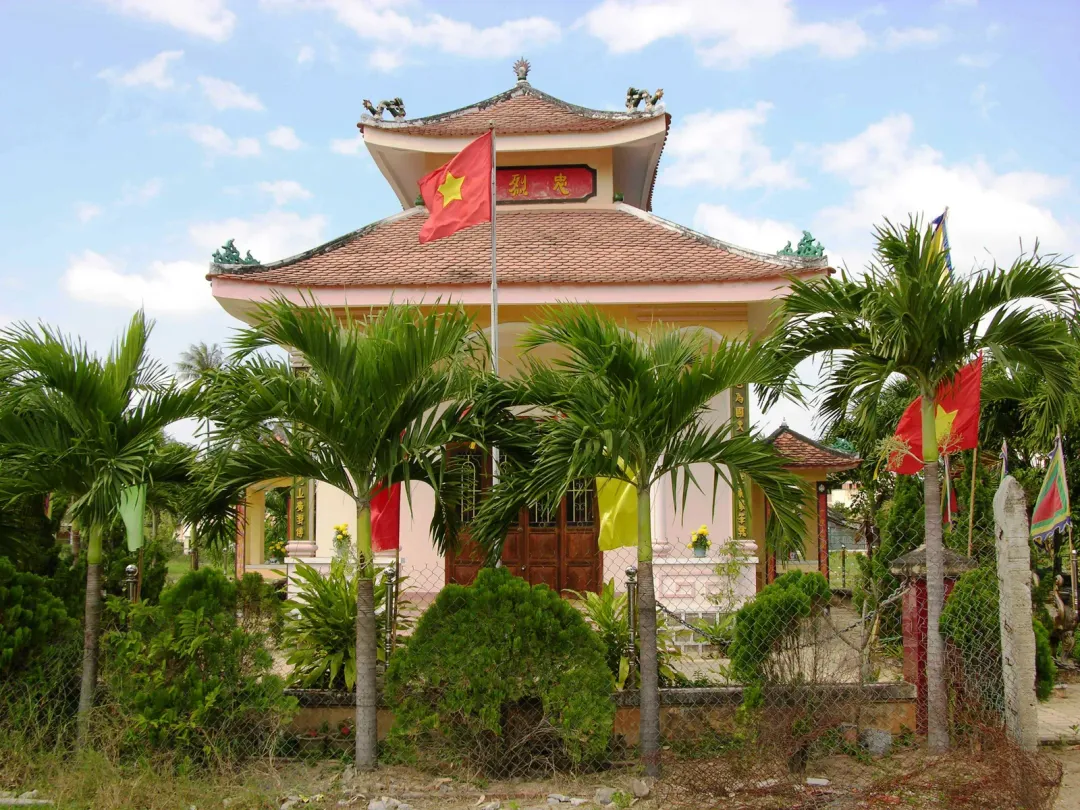 The Trần Quý Cáp memorial temple at Diên Khánh seen from the fence, flags and palms in the yard