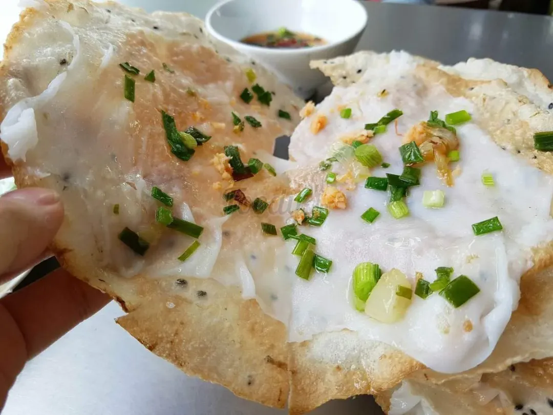 Bánh đập held up. A sesame rice cracker under a sheet of steamed rice, scattered with spring onion and crisp shallot